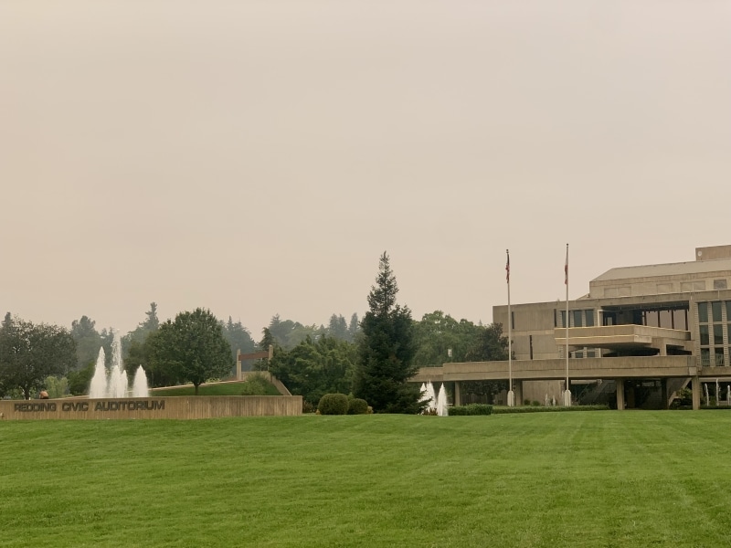 big concrete building with flags against green gas background with fountain in distance, skies are grey