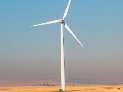 tall white wind turbine against blue sky with brown grass around it