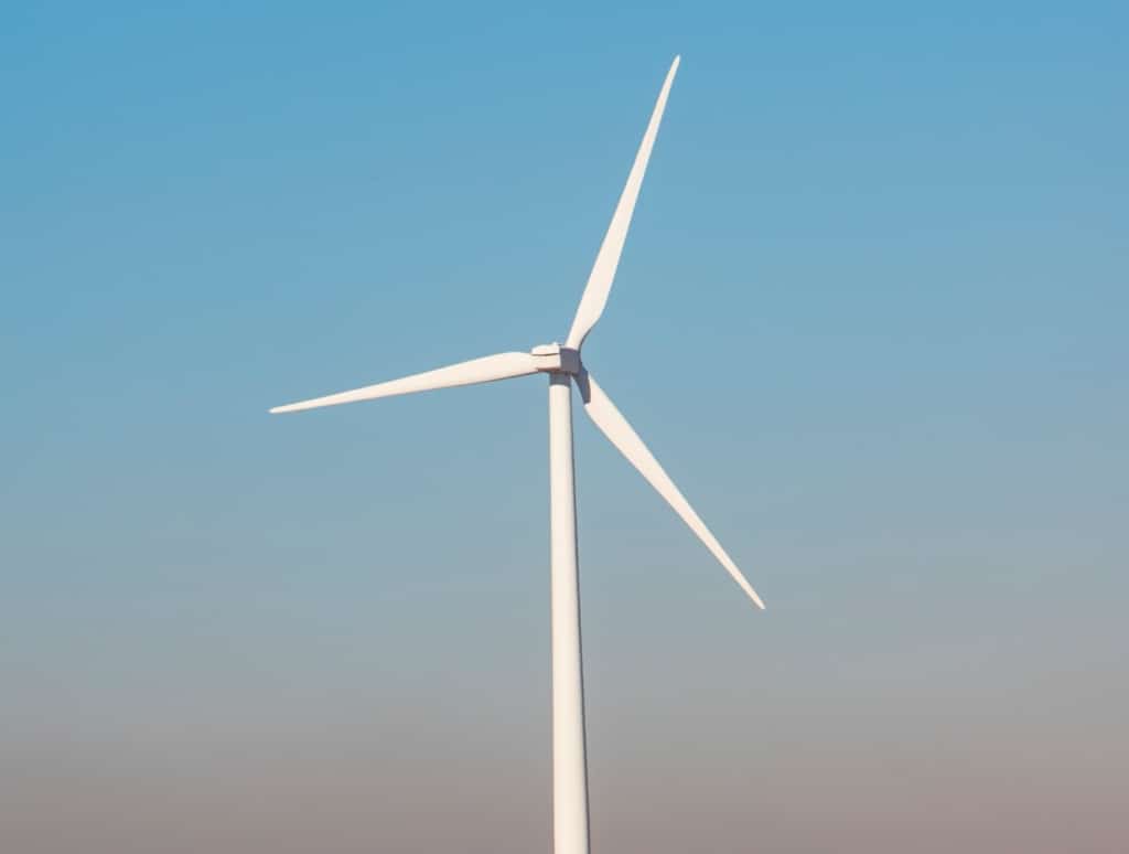 tall white wind turbine against blue sky with brown grass around it