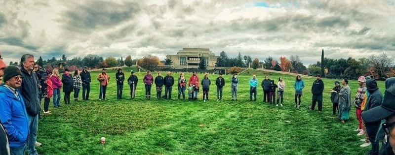 Indigenous Peoples gather in circle on green lawn at sunrise