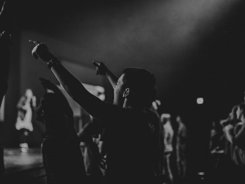 black and white image with young man's back to camera and arms raised in worship